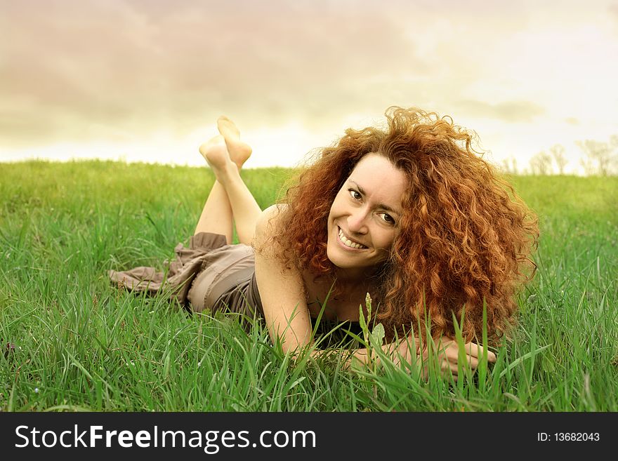 Smiling red haired woman lying on a green meadow. Smiling red haired woman lying on a green meadow