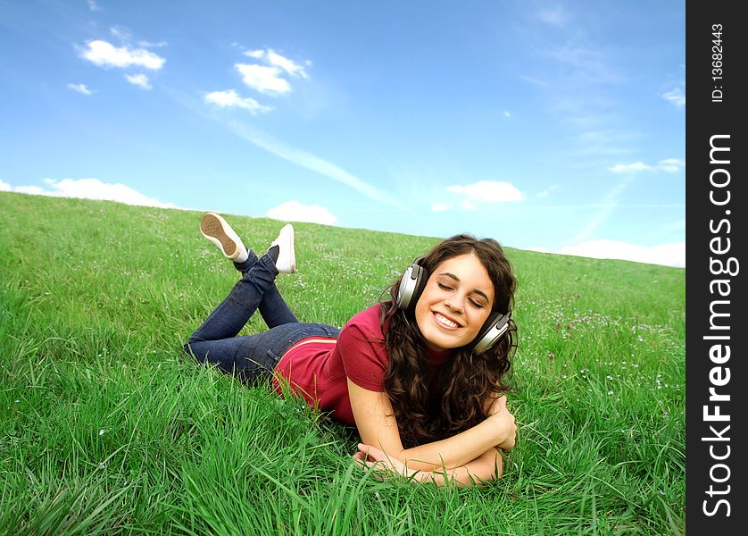 Smiling young woman lying on a green meadow and listening to music. Smiling young woman lying on a green meadow and listening to music
