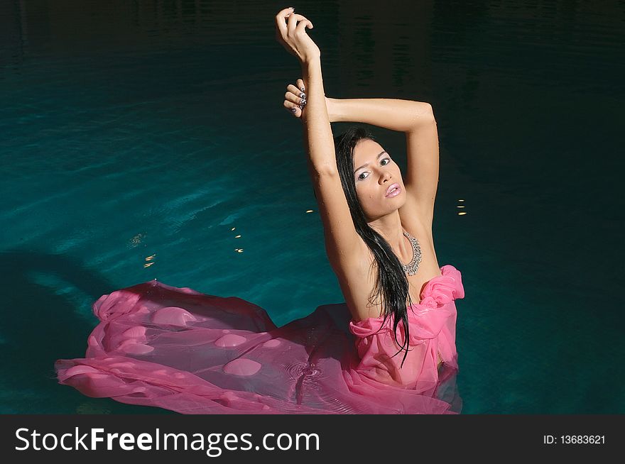 The girl in a pink fabric, costs in pool and holds hands above. The girl in a pink fabric, costs in pool and holds hands above
