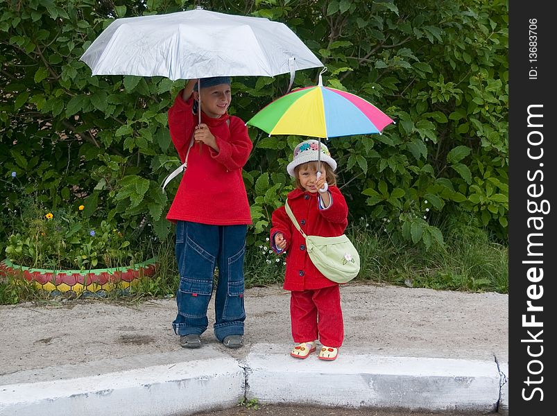 The boy and the girl stand with umbrellas. The boy and the girl stand with umbrellas