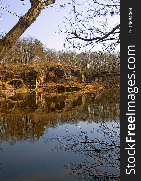 Cliff with trees and shrubs in the spring at a pond with reflections. Cliff with trees and shrubs in the spring at a pond with reflections.