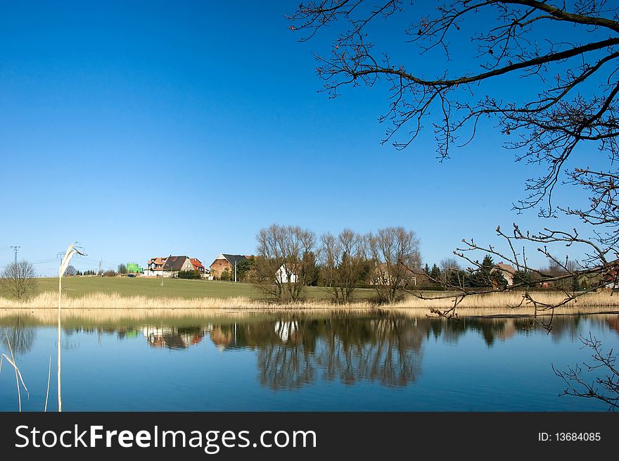 Small village at the lake bank in the spring sun with reflection on the water surface.