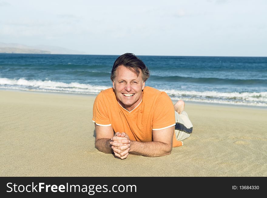 A colour portrait photo of a happy smiling forties man laying on a beautiful sandy beach.