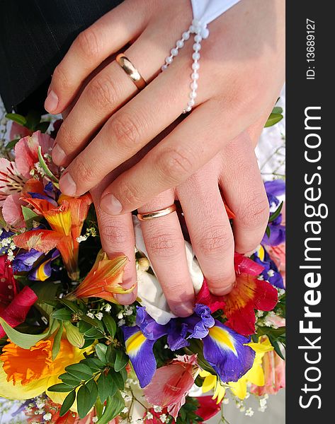 Hands of the groom and the bride with wedding rings on top of the bride's bouquet