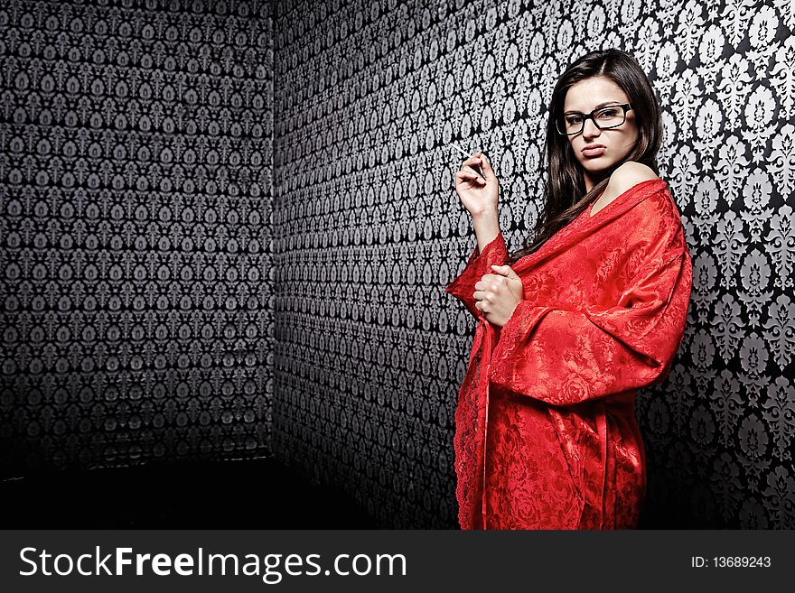 The attractive girl in red with a cigarette against a black wall with an ornament. The attractive girl in red with a cigarette against a black wall with an ornament