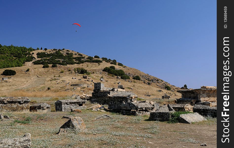 A paraglider is flying over ancient town of Hierapolis in Turkey in the background of the blue sky. A paraglider is flying over ancient town of Hierapolis in Turkey in the background of the blue sky.