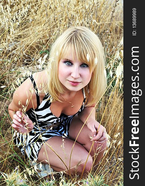 Blonde girl sitting in the dry grass. Blonde girl sitting in the dry grass