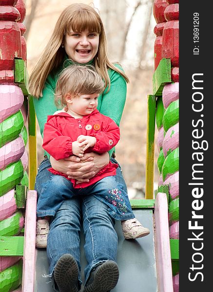 A young woman sitting at the top of a slide with a little girl on her knees at a playground. A young woman sitting at the top of a slide with a little girl on her knees at a playground