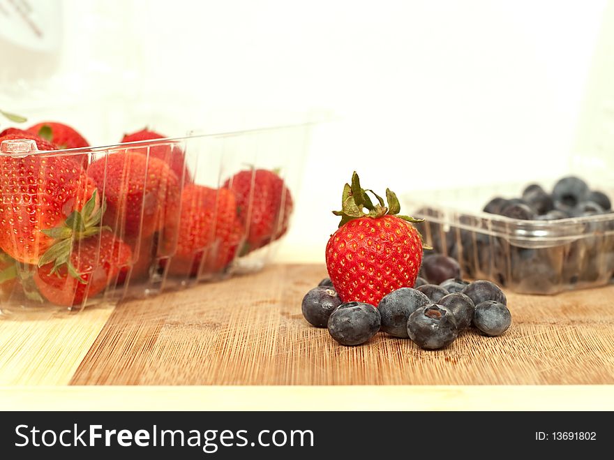 Strawberries and Blueberries on a wooden cutting board in and out of plastic containers.