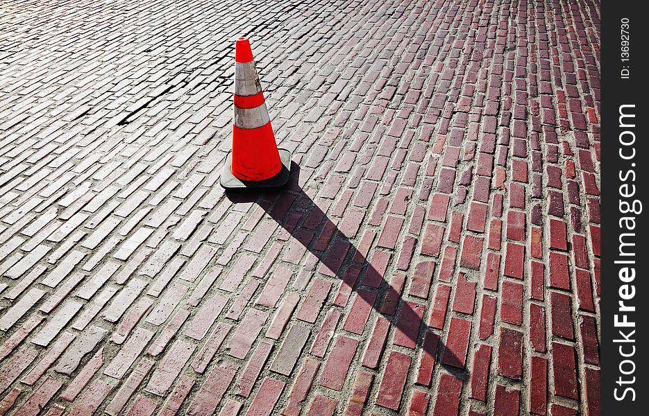 Traffic cone and long shadow on brick street. Traffic cone and long shadow on brick street