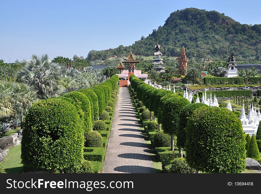 Clipped bushes line a pathway leading to one of the Thai viewing pavilions overlooking the formal French garden and its white Chedis and distant pagoda towers at Nong Nooch Tropical Gardens in Pattaya, Thailand. Clipped bushes line a pathway leading to one of the Thai viewing pavilions overlooking the formal French garden and its white Chedis and distant pagoda towers at Nong Nooch Tropical Gardens in Pattaya, Thailand.