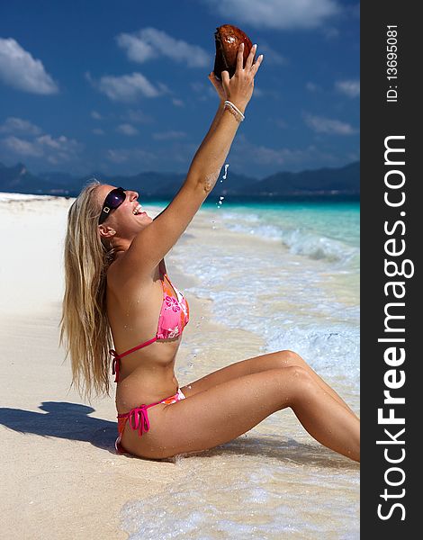 Caucasian blond woman on tropical beach pouring water from coconut shell. Caucasian blond woman on tropical beach pouring water from coconut shell