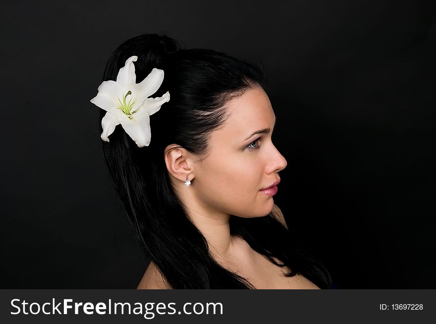 Beautiful woman with a white lily in dark hair, a portrait on a black background.