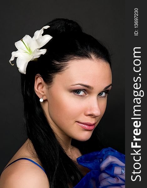 Beautiful woman with a white lily in dark hair, a portrait on a black background.