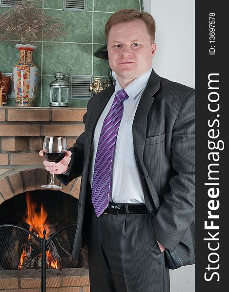 The man in a fashionable suit with a glass of red wine at a fireplace. The man in a fashionable suit with a glass of red wine at a fireplace.
