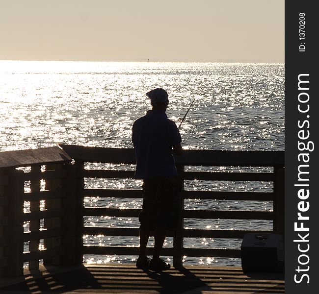 The silhouette of a fisherman at a pier against the glow of the setting sun. The silhouette of a fisherman at a pier against the glow of the setting sun.