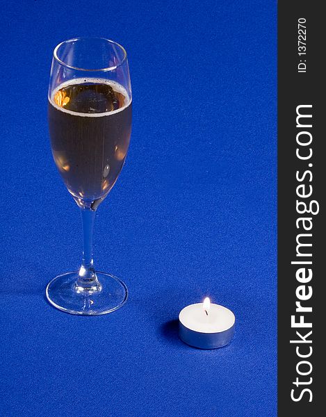 A glass of champagne with candle on blue background