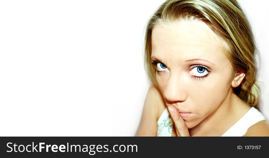 A young blond woman with blue eyes in front of white background is holding her finger in front of her mouth. A young blond woman with blue eyes in front of white background is holding her finger in front of her mouth