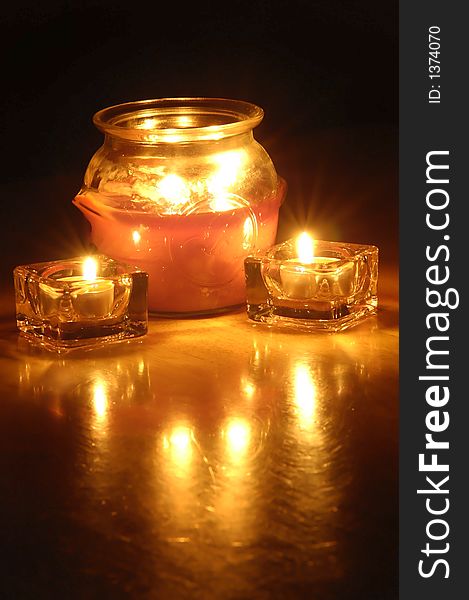 Several candles glowing with dark background and reflections on wood
