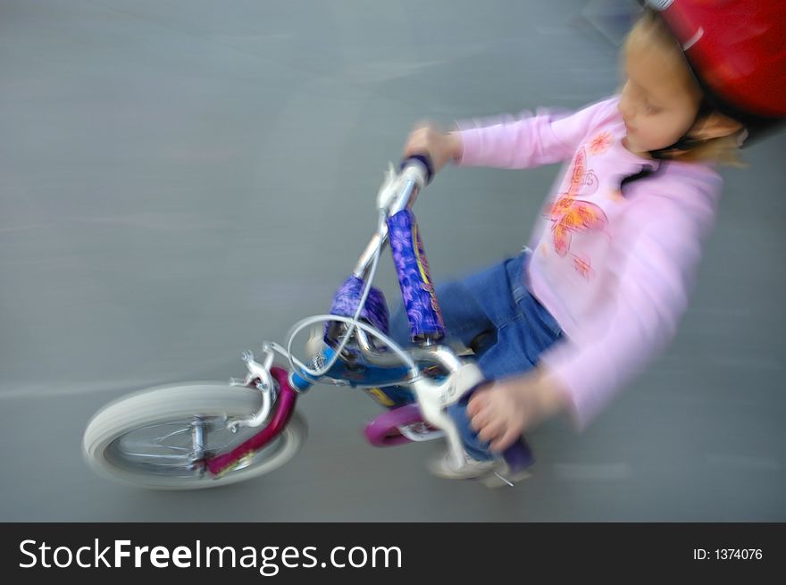 Motion shot of little girl biking with red helmet