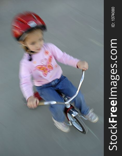 Motion shot of little girl biking with red helmet