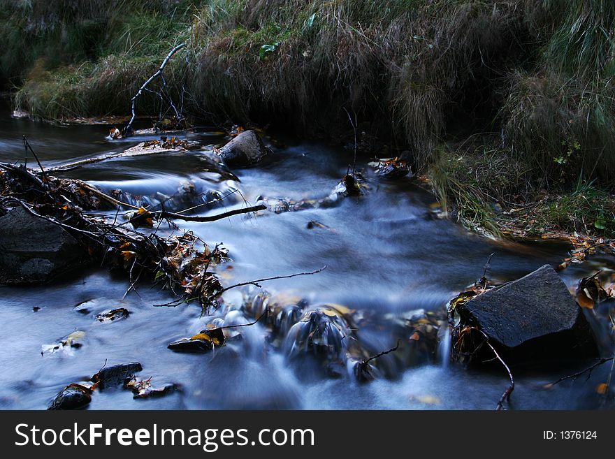 A small stream in autumn, fluid motion in streaming water, which is full of fallen leaves and branches. A small stream in autumn, fluid motion in streaming water, which is full of fallen leaves and branches.