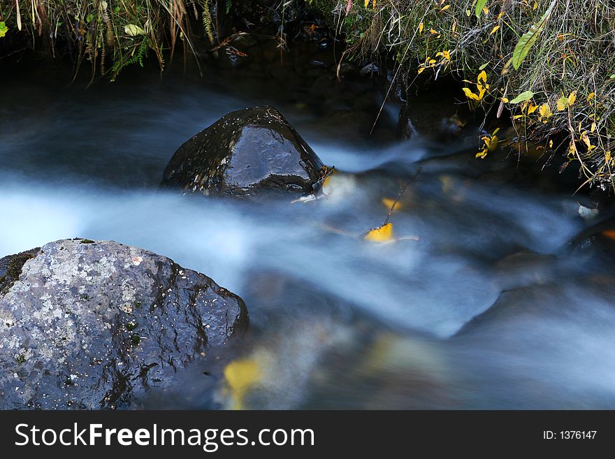 Two rocks in a small stream, motion to streaming water, leaves and branches in the water. Picture taken in autumn