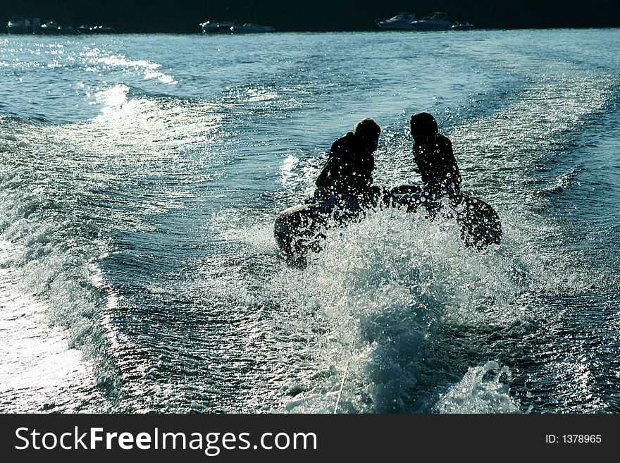 Silhoette of two girls tubing on lake.