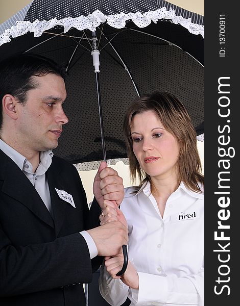 Fired man and woman showing identical situation and staying under the same umbrella. Fired man and woman showing identical situation and staying under the same umbrella