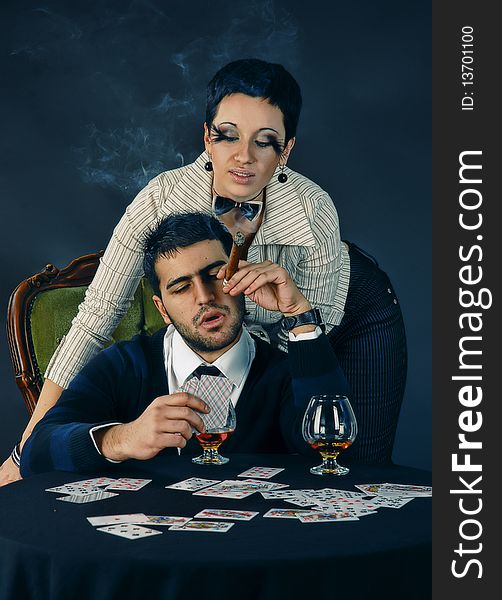 There is cool couple. He smokes cigar and holds cards. There is cool couple. He smokes cigar and holds cards.