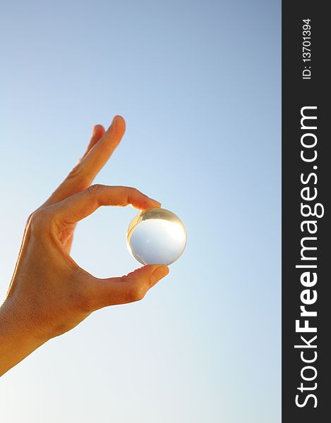 Woman's hand holding a clear ball against the blue sky. Woman's hand holding a clear ball against the blue sky.