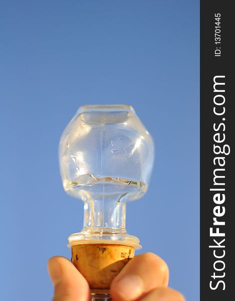A glass stopper with a cork bottom held up against a clear blue morning sky reflecting glints of sunlight. A glass stopper with a cork bottom held up against a clear blue morning sky reflecting glints of sunlight.
