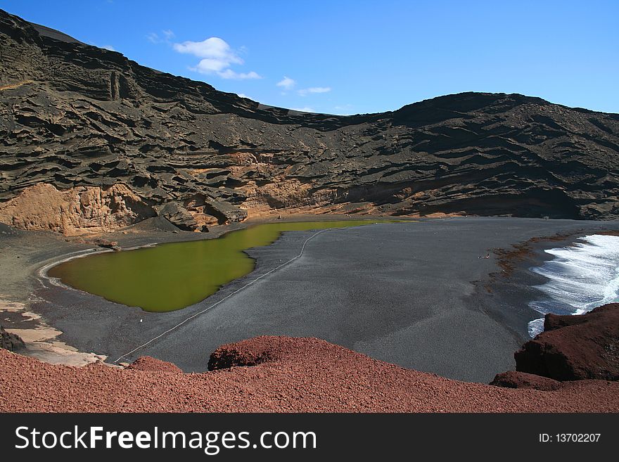 Green lake on the beach with dark lava sand - seaside of island Lanzarotte, Spain, Europe. Green lake on the beach with dark lava sand - seaside of island Lanzarotte, Spain, Europe