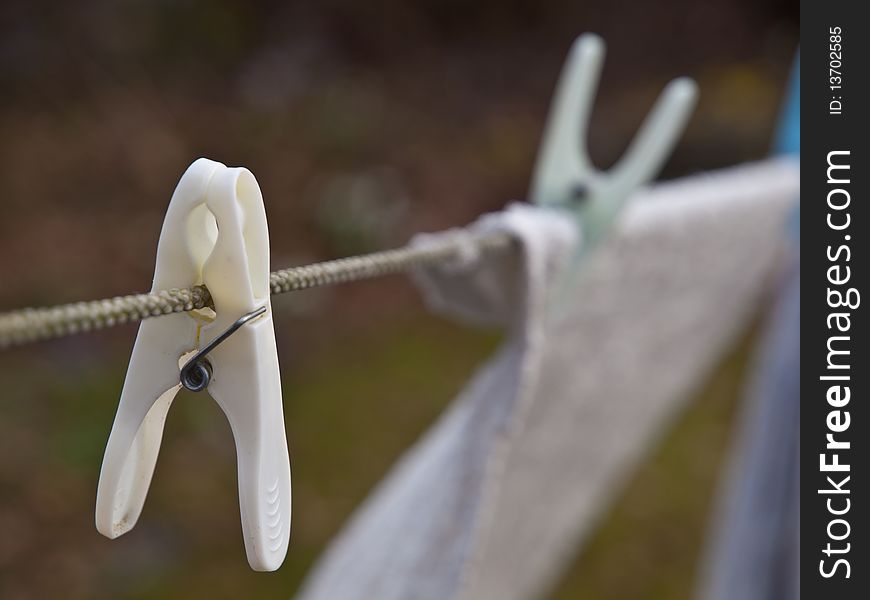 White clothespin on clothes line with laundry in background.