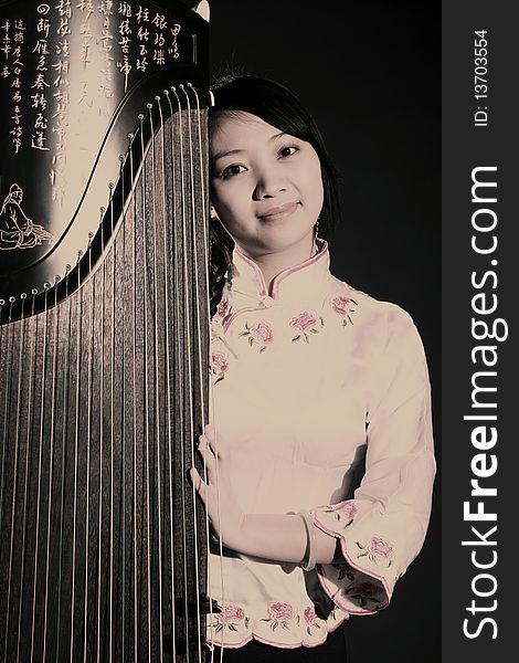 Chinese zither performer in traditional dress with her zither on dark. Chinese character on zither is Chinese Tang poetry,also a famous Tang Dynasty poet's calligraphy. It praised the unique charm of the zither.