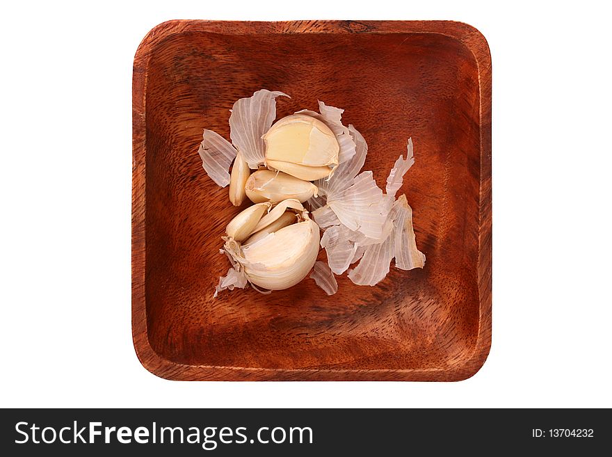 Garlic segments in a peel on a wooden square plate.