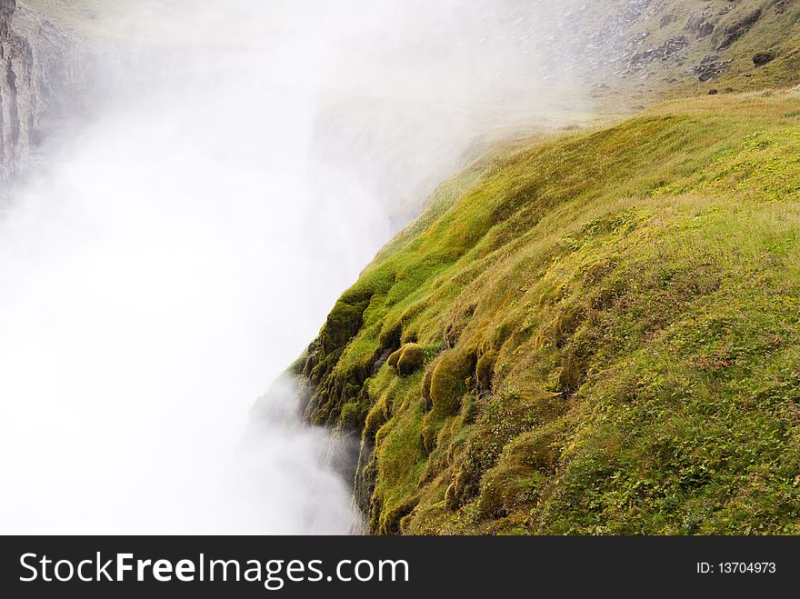 Detail of the Gullfoss waterfall in Iceland, wild water mist with mountains of green grass and moss