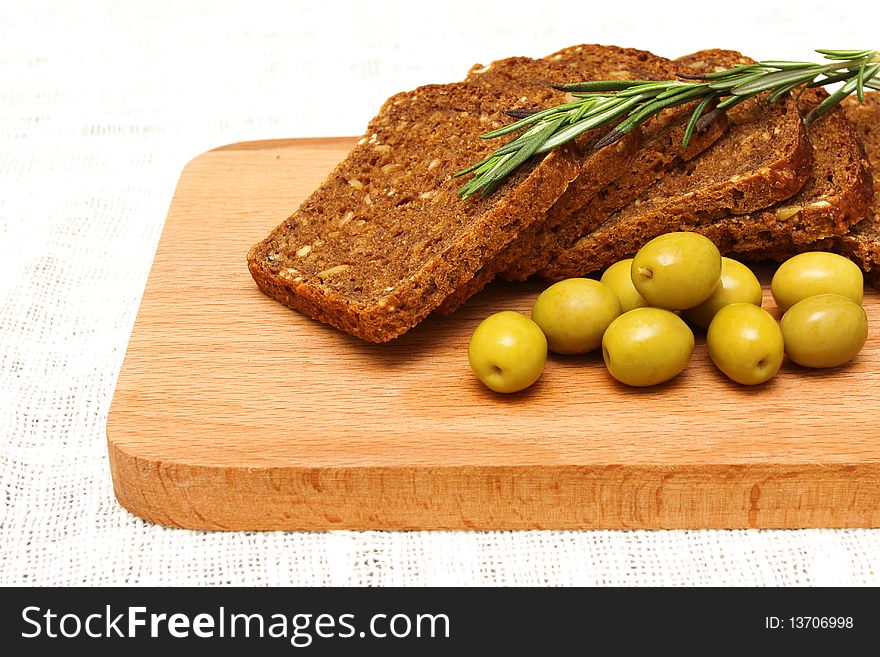 Bread, green olives and rosemary on a wooden board on the white linen tablecloths. Bread, green olives and rosemary on a wooden board on the white linen tablecloths