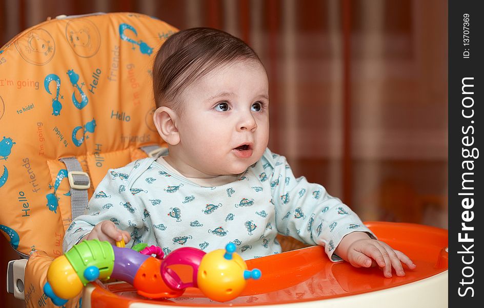 Half-year-old kid sitting on a chair for feeding and playing. His playful mood, but he was surprised. Half-year-old kid sitting on a chair for feeding and playing. His playful mood, but he was surprised