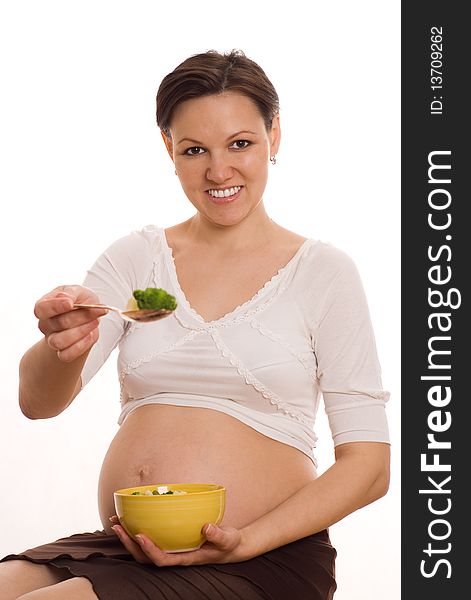 Beautiful pregnant woman eats vegetables on white. Beautiful pregnant woman eats vegetables on white