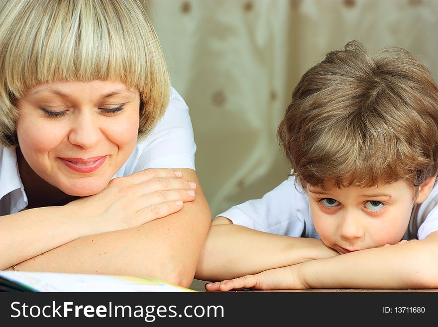 Woman and little boy lying down on the floor and reading a book. Woman and little boy lying down on the floor and reading a book