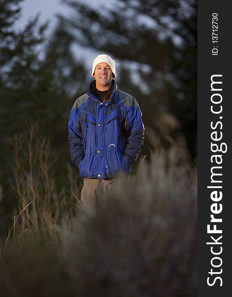 Portrait of a smiling man standing in a clearing in the wilderness. He is wearing a coat and hat. Vertical format. Portrait of a smiling man standing in a clearing in the wilderness. He is wearing a coat and hat. Vertical format.