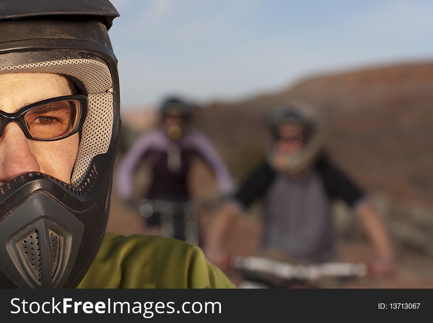 Closeup and cropped view of a male mountain biker in a helmet and protective eyewear. In the background are two other bikers. Horizontal shot. Closeup and cropped view of a male mountain biker in a helmet and protective eyewear. In the background are two other bikers. Horizontal shot.