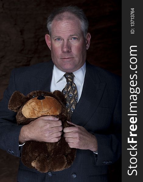 A businessman is clutches on to a teddy bear for security with a dark and rocky landscape in the background. Vertical shot. A businessman is clutches on to a teddy bear for security with a dark and rocky landscape in the background. Vertical shot.