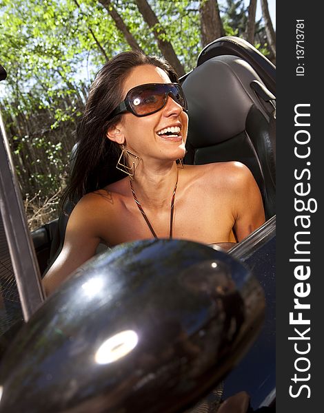 Tilt view of an attractive young woman in sunglasses driving a convertible. She is smiling and looking out the side of the car. Vertical format. Tilt view of an attractive young woman in sunglasses driving a convertible. She is smiling and looking out the side of the car. Vertical format.