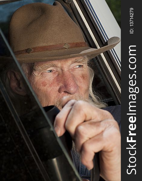 Cropped close-up of an elderly man with a cowboy hat and white beard, driving a pickup truck and staring out the window. Vertical format. Cropped close-up of an elderly man with a cowboy hat and white beard, driving a pickup truck and staring out the window. Vertical format.