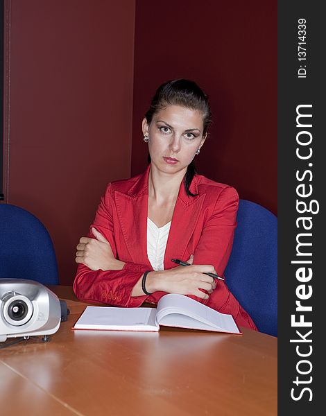 Attractive young businesswoman in a red blazer sits with her arms crossed and wears a serious expression on her face. Vertical shot.