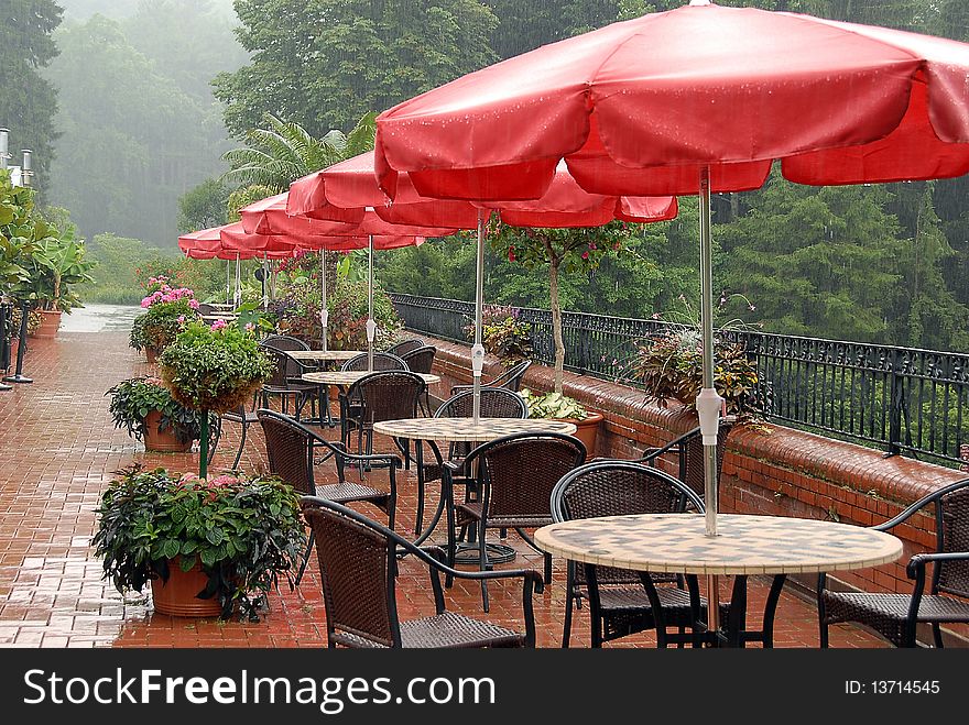 Patio tables with red umbrellas during the rain