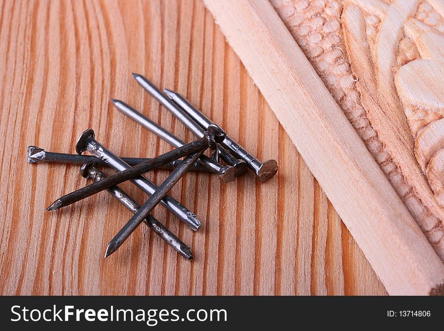 Nails for building and repair work, nearby a wooden board with a decorative carving.