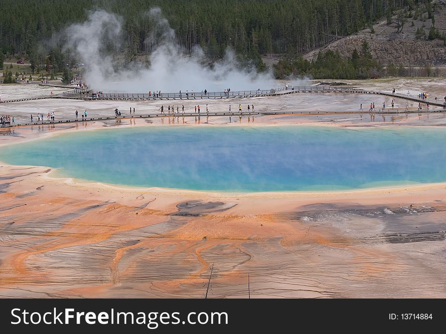 Tourists walk along wooden boardwalks surrounding Grand Prismatic geyer basin in Yellowstone Park as seen from a nearby hilltop. Tourists walk along wooden boardwalks surrounding Grand Prismatic geyer basin in Yellowstone Park as seen from a nearby hilltop